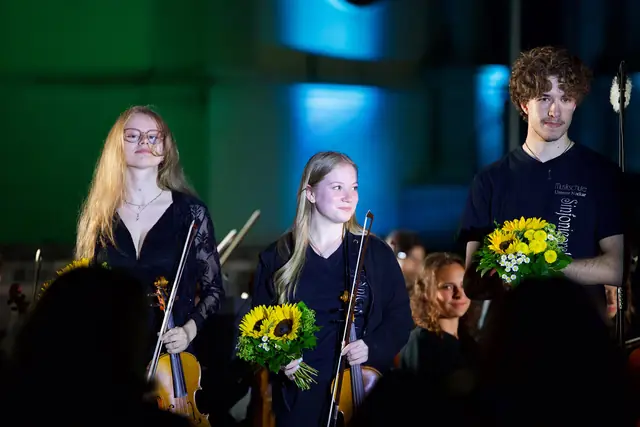 Zwei junge Solistinnen mit Sonnenblumen und ein Schüler mit Blumenstrauß nach dem Konzert