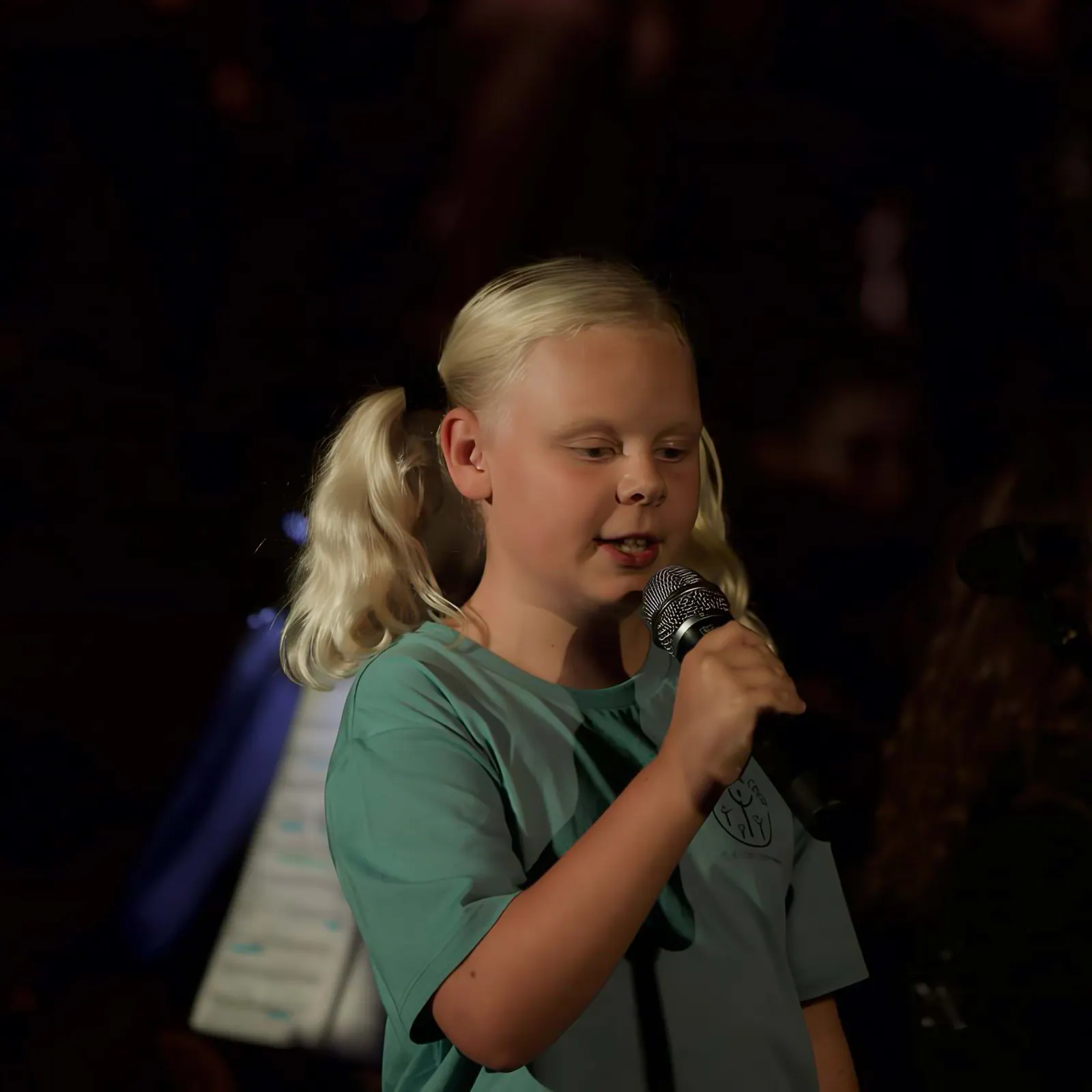 Ein Mädchen singt ein Solo ins Mikrofon, hinter ihr das Orchester