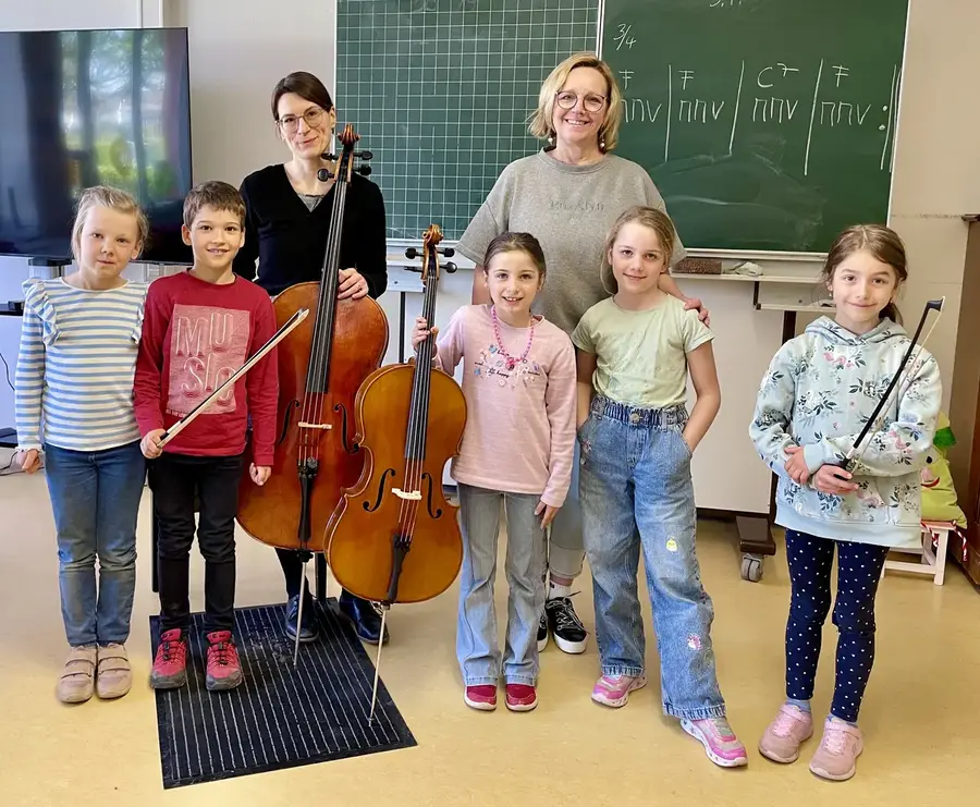 Grundschulkinder mit Geige und Cello und zwei Lehrerinnen der Musikschule im Klassenzimmer