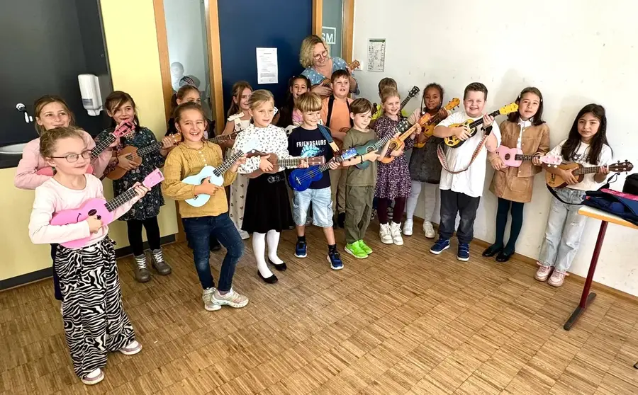 Eine Grundschulklasse mit bunten Ukulelen und ihrer Lehrerin bei der Einschulungsfeier