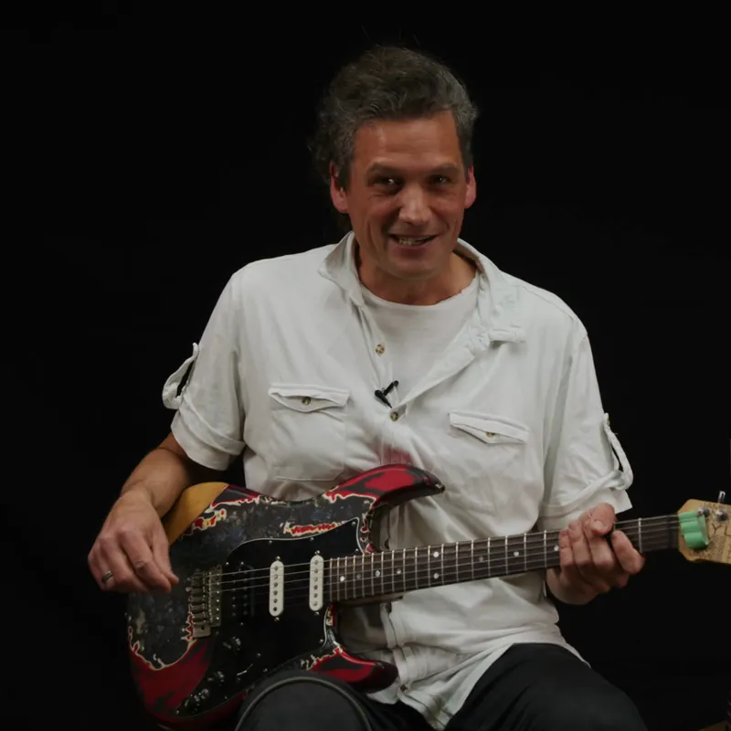 Alexander Strobel lacht mit seiner E-Gitarre im Arm